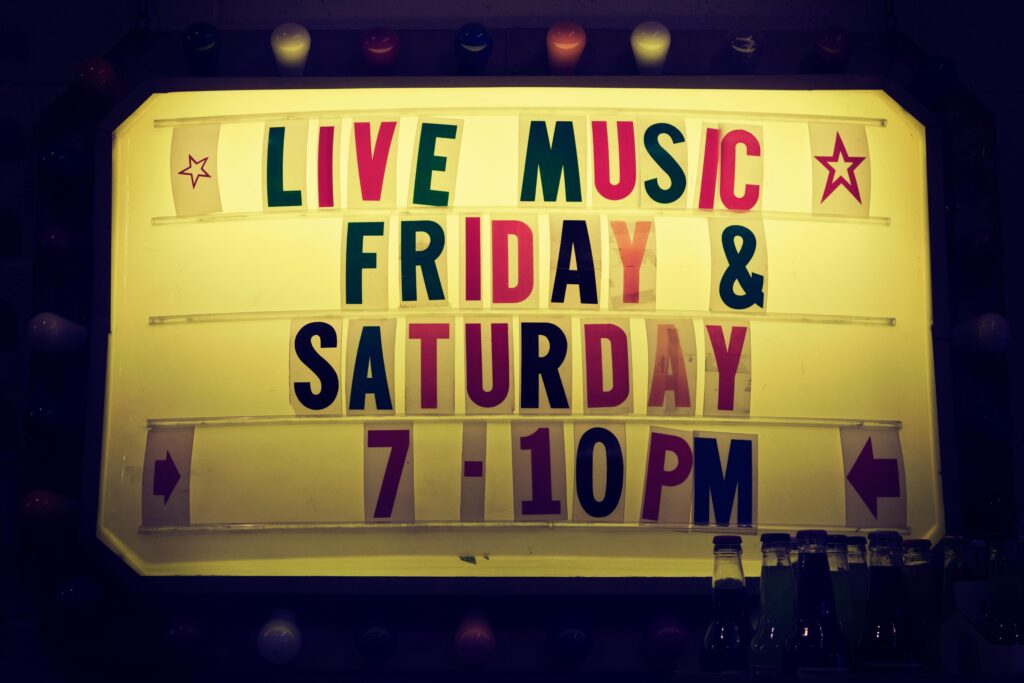 An outdoor sign at a dive bar that says 'Live Music Friday & Saturday 7-10PM in block letters that don't match. 