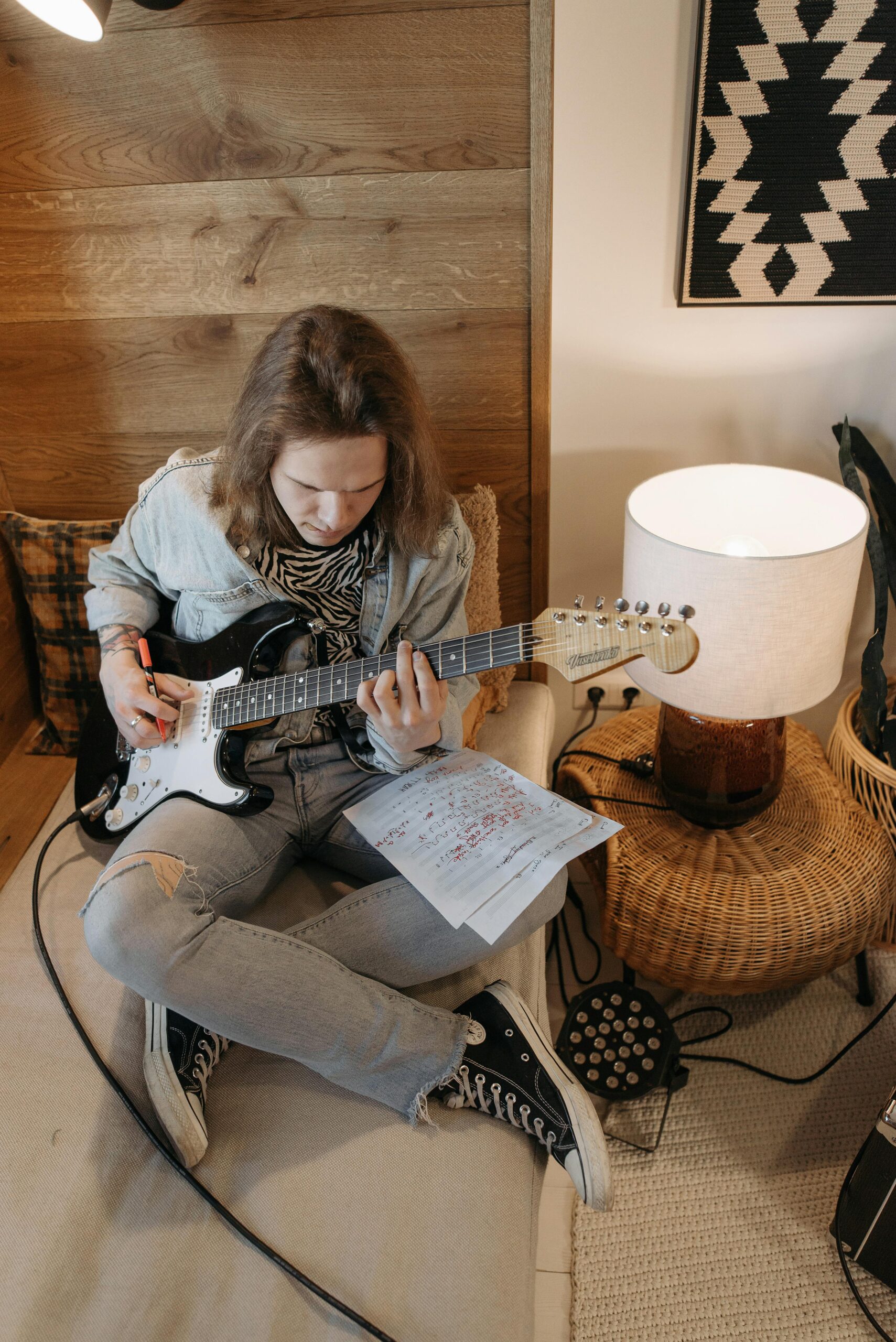 A man sitting cross legged with sheet music on his lap playing an electric guitar.
